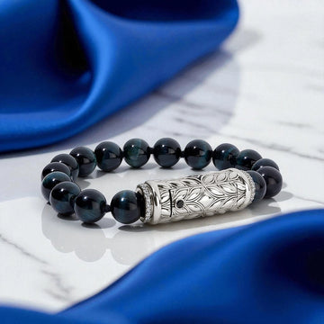 Sterling silver detailed bead bracelet with deep blue tiger’s eye stones and diamond accents, elegantly styled on white marble with a rich blue silk drape background.