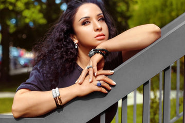 Elegant woman showcasing a silver sapphire ring, mixed-metal bracelets, and gemstone drop earrings by Daneila Léon — styled outdoors with soft natural light and a confident gaze.