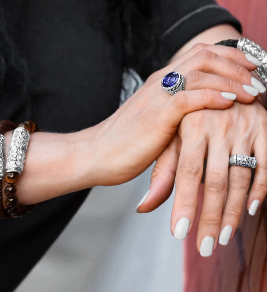 Close-up of a woman’s hands adorned with silver rings and bracelets featuring blue gemstones, against a soft blurred background.