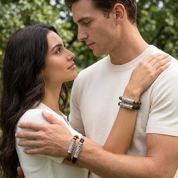 Couple standing closely together in a green park, both wearing Persian Shield silver bracelets paired with tiger-eye stones and black leather. The man wears two stacked bracelets while the woman’s hand rests on his shoulder, highlighting the engraved Persian Shield silver design.