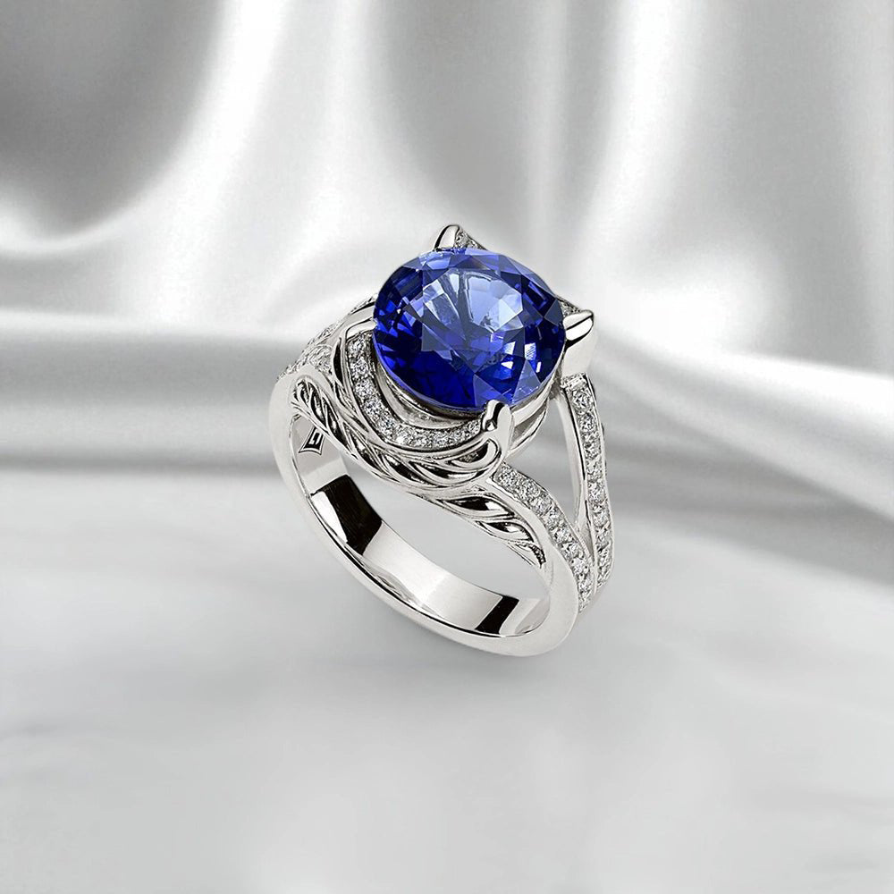 Silver ring with a round brilliant-cut blue sapphire center stone, accented by pave lab-grown diamonds on a sculptural Persian Shield design, shown on a white satin background.