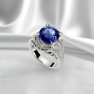 Silver ring with a round brilliant-cut blue sapphire center stone, accented by pave lab-grown diamonds on a sculptural Persian Shield design, shown on a white satin background.