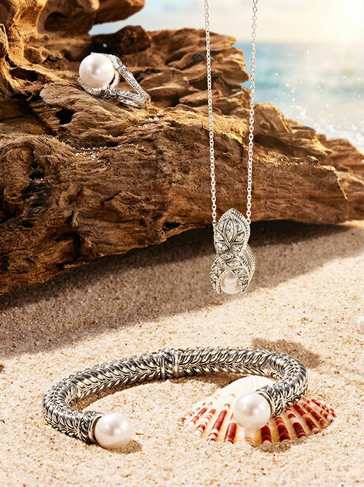 Sterling silver Persian shield leaf jewelry set featuring a pearl bracelet, pendant necklace, and ring, styled on coastal sand and weathered rock in natural sunlight.