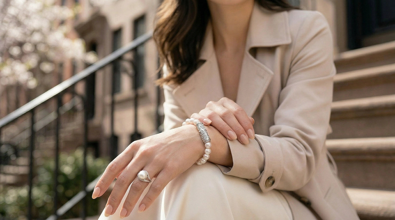 Elegant woman seated on city steps wearing a sterling silver pearl bracelet and matching pearl ring, hands relaxed in soft natural lightslider_item_UFaDBy