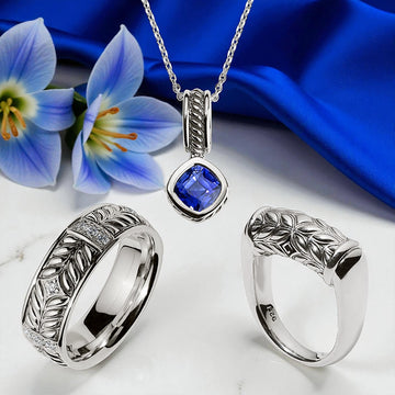 Handcrafted sterling-silver jewelry from Daneila Léon — a sapphire pendant and sculptural silver rings displayed on marble with blue satin and floral accents, embodying quiet luxury and modern craftsmanship.