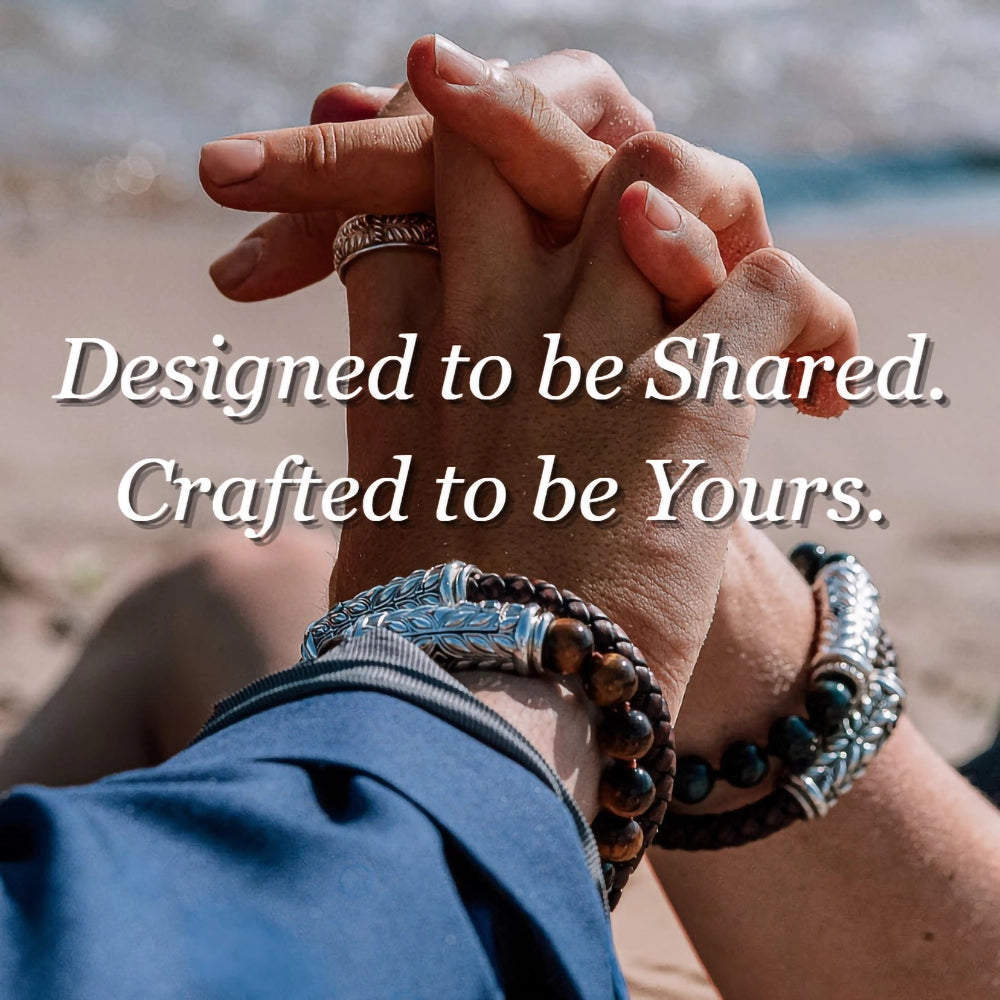 Close-up of two hands clasped together on a beach, both wearing Persian Shield silver and gemstone bracelets. Text overlay reads “Designed to be Shared. Crafted to be Yours.”