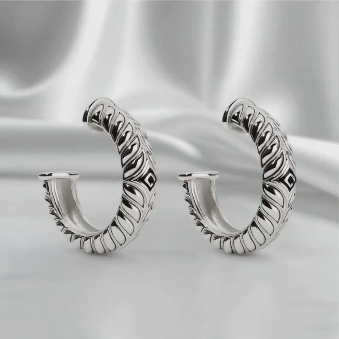 Sterling silver Persian Shield hoop earrings shown on a soft satin backdrop, rotating gently under studio lighting to highlight sculpted detail and polished finish.